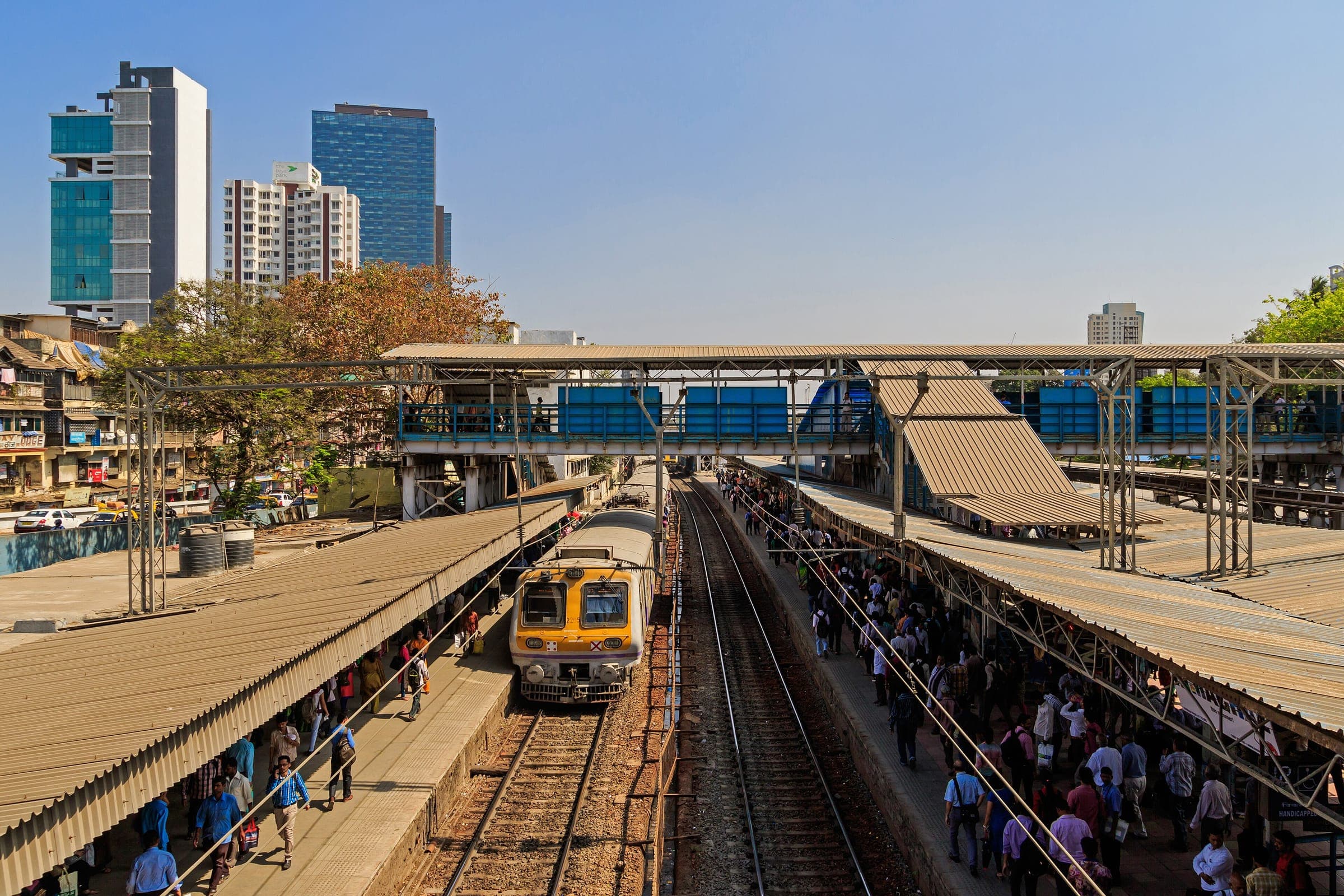 A local train pulling into Dadar station beside crowded platforms