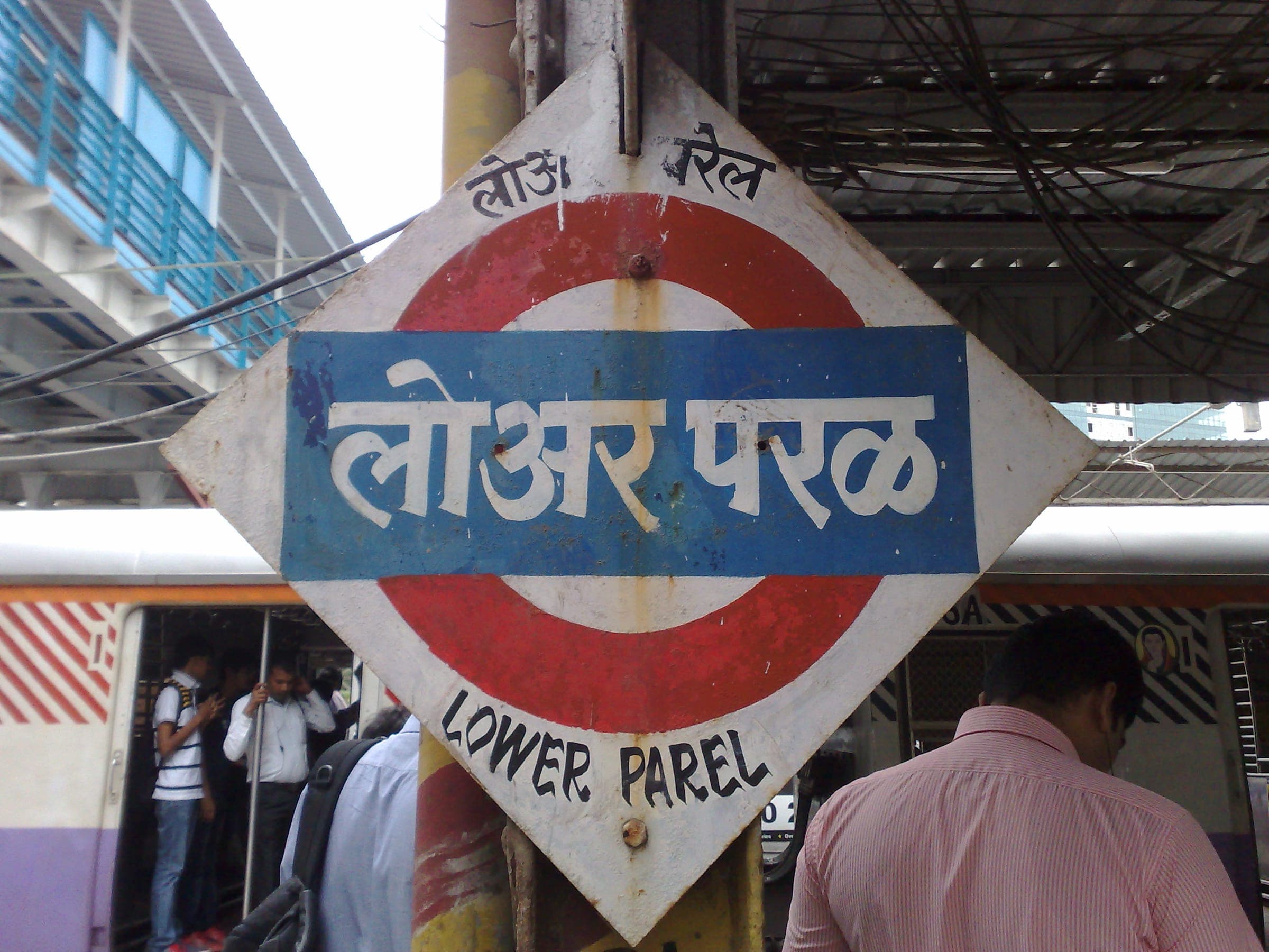 The Lower Parel station name board in Devanagari and English, with a local train behind it