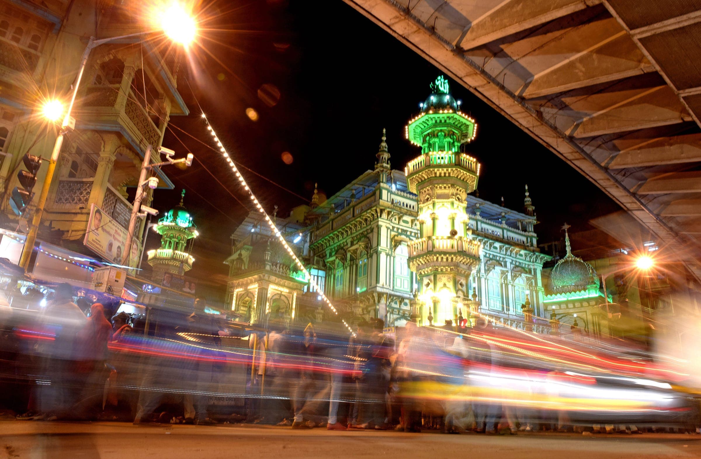 Minara Masjid lit in green at night, traffic streaking past under the flyover