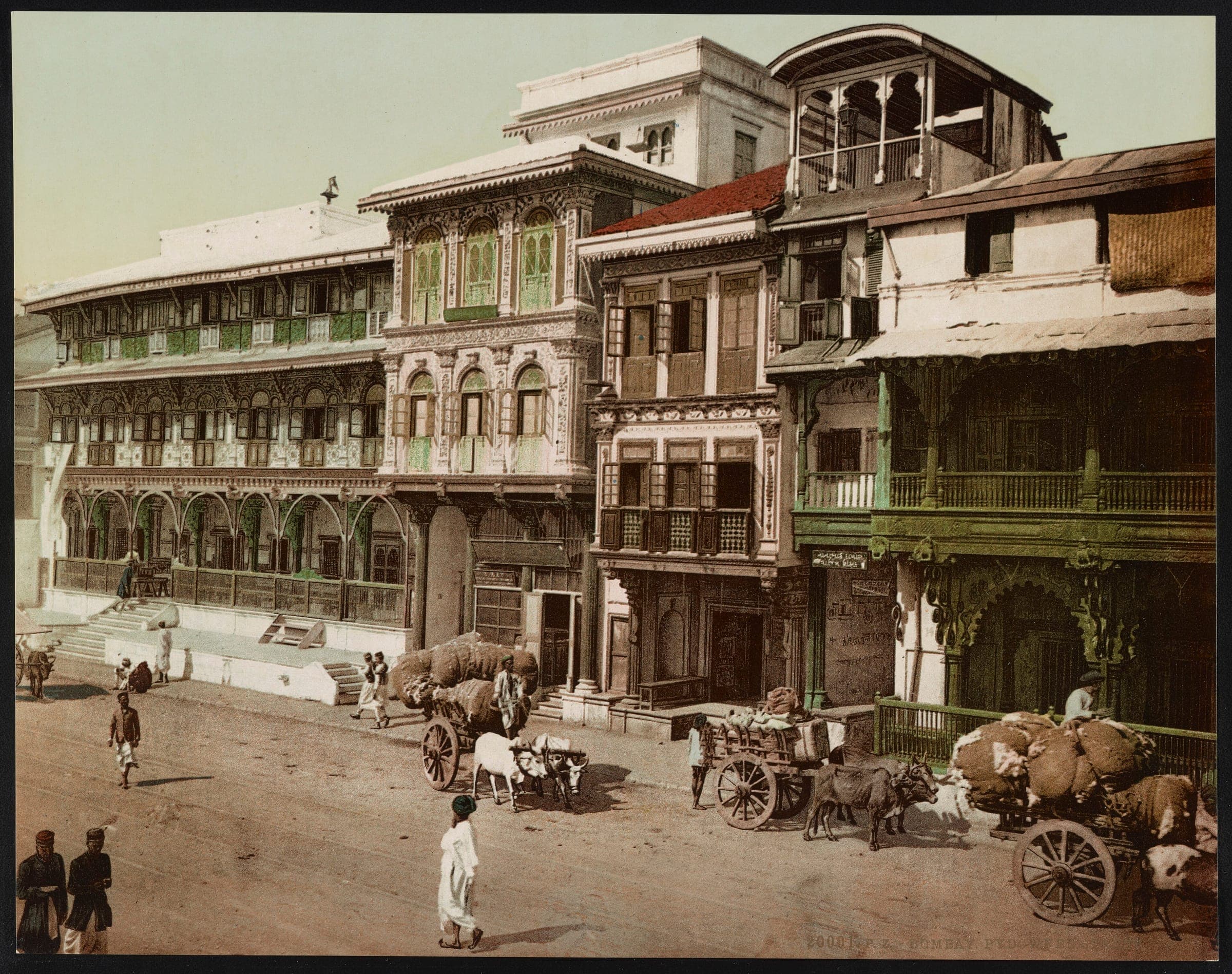 Bullock carts loaded with sacks outside carved wooden-balconied houses on Pydhonie Street in the 1890s