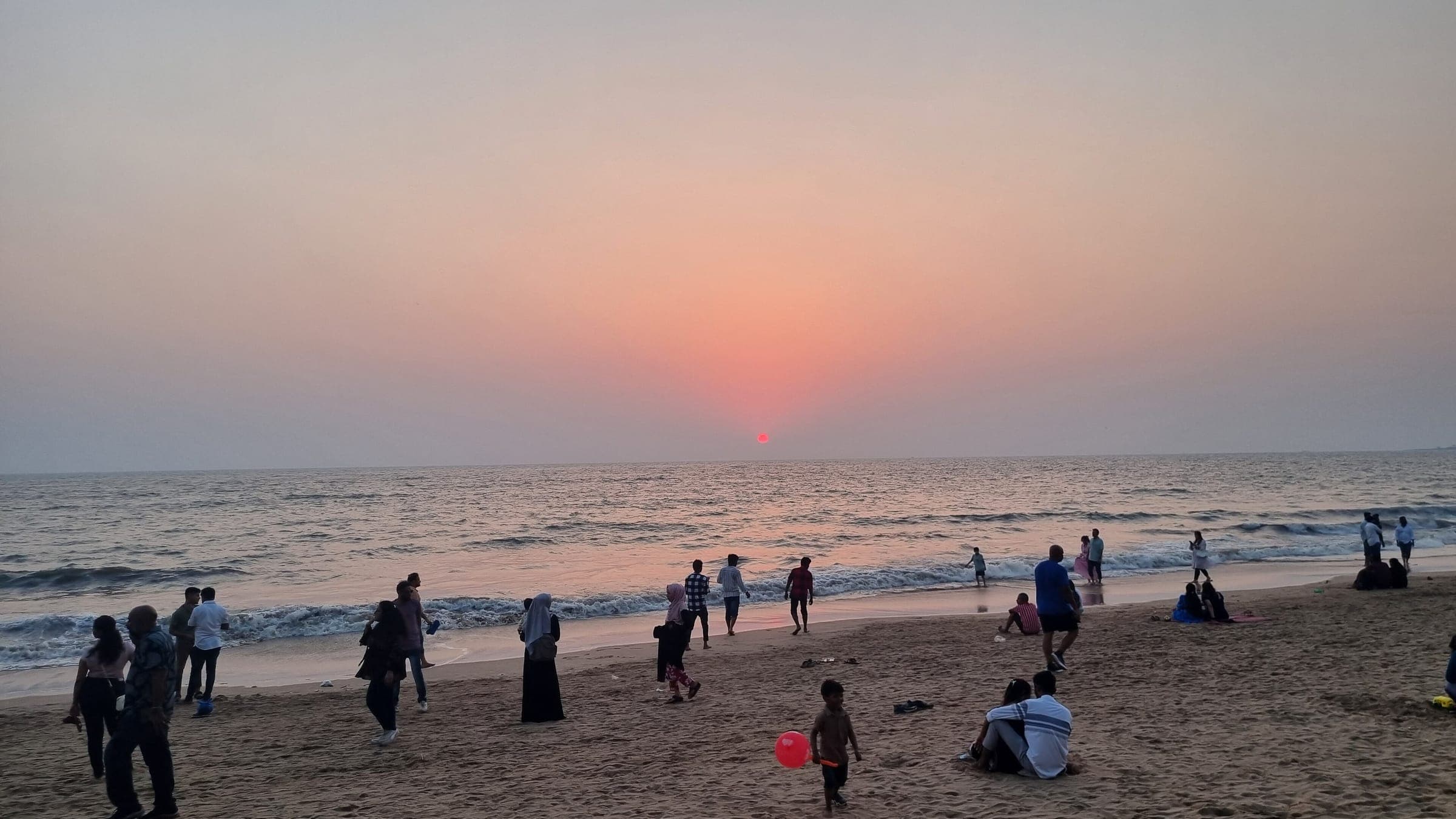 People on Juhu Beach at sunset, the sun low over the sea